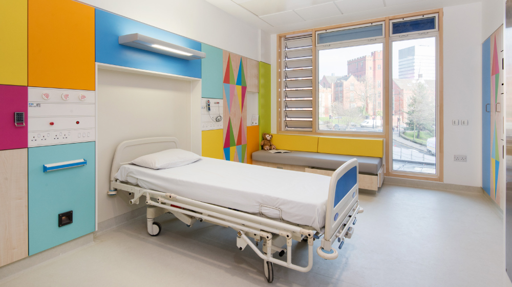 Uma cama em um ambiente hospitalar com as paredes repletas de formas coloridas